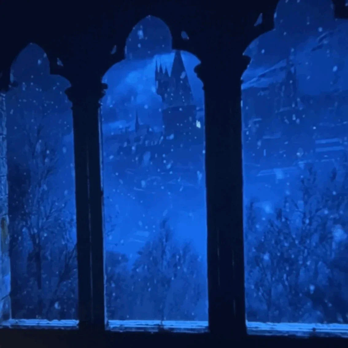 Snow falling outside a castle window with gothic arches at night